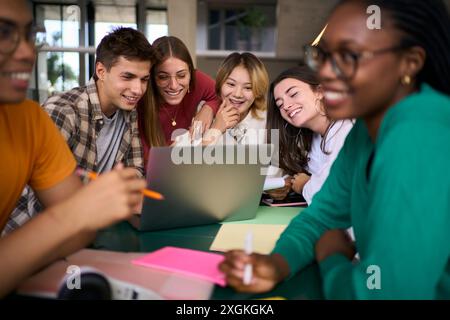 Group of young university students people gathered using laptop together in campus study hall. Stock Photo