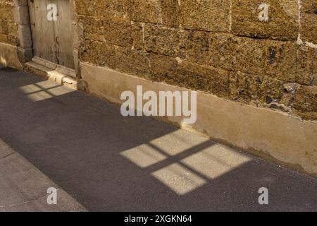 A long shadow from a window falls across the cobblestone street in Langeac, France, creating a captivating interplay of light and shadow. Stock Photo