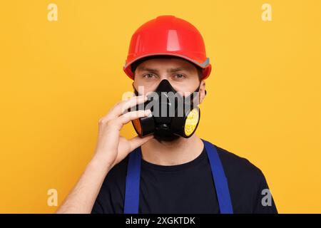 Man in respirator mask and hard hat on yellow background Stock Photo