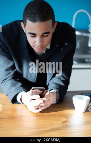 Serious young businessman using smartphone indoors, browsing internet and checking messages in natural light Stock Photo