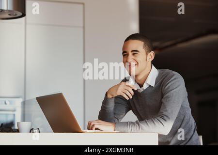 Young professional is working remotely, enjoying the comforts of his modern kitchen as he tackles his tasks with a positive attitude Stock Photo