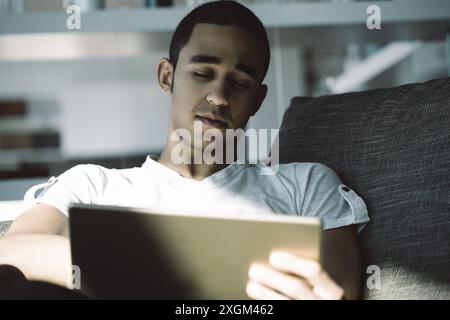 Young man browsing the internet on his tablet in a cozy modern home, showcasing technology integration in everyday life Stock Photo