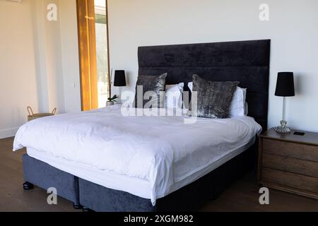 A neatly made bed with plush pillows in a modern bedroom. The room's decor suggests a minimalist style with a focus on comfort and elegance. Stock Photo
