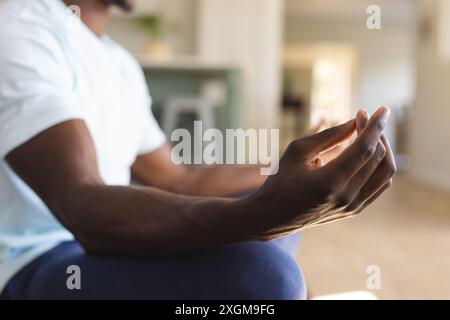 Midsection of african american man practicing yoga meditation sitting on floor at home. Lotus position, yoga, meditation, wellbeing, domestic life and Stock Photo