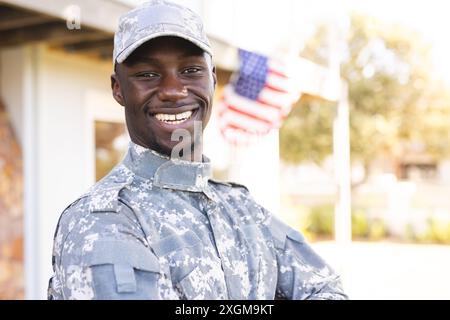 Portrait of happy african american male soldier in uniform standing outside home smiling, copy space. Military service, army, home, domestic life and Stock Photo