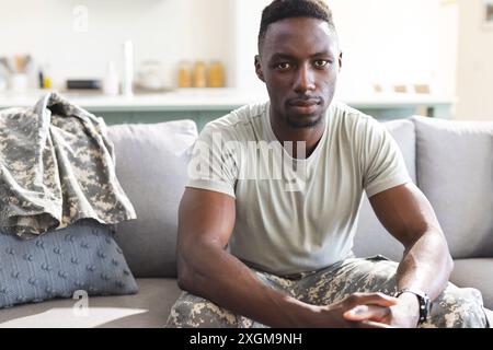 Portrait of serious african american male soldier sitting on couch at home. Depression, ptsd, military service, army, return, home, mental health and Stock Photo