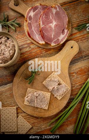 Two crackers topped with savory ham pate, adorned with rosemary, on a rustic wooden board Stock Photo