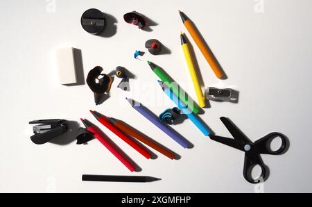 Photo of office equipment. Scattered randomly on a white background. Colored pencils, scissors, stapler, eraser, pencil sharpeners. Pieces of twisted Stock Photo
