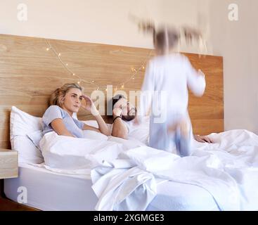 Parents, bed and tired from jumping child, adhd and chaos in home bedroom on weekend. Excited, energy and girl with motion blur for speed, headache Stock Photo