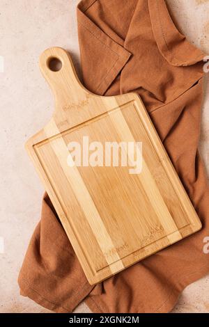 Cutting board, beige, unpainted, with a kitchen towel, on a beige background, top view Stock Photo