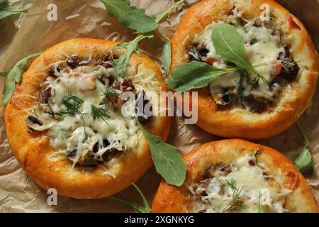 Three mini pizzas topped with mushrooms, melted cheese, and garnished with arugula on parchment paper Stock Photo