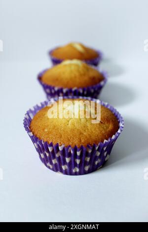 Three cupcakes in purple liners arranged in a row on a white surface Stock Photo