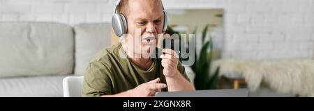A man with inclusivity in casual attire sits at a desk in his home studio, wearing headphones, and ready to work. Stock Photo