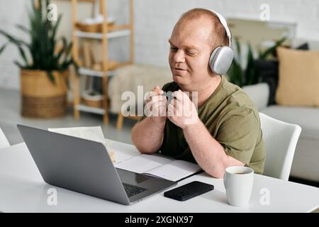A man with inclusivity wearing headphones sits at a desk in his home office, working on a laptop. Stock Photo