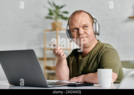 A man with inclusivity wearing headphones sits at his desk in his home office working. Stock Photo