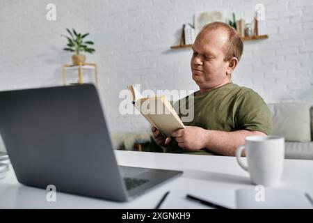 A man with inclusivity sits at a desk in his home, reading a book. Stock Photo