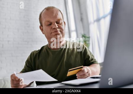 A man with inclusivity in casual attire sits at a desk, reviewing bills and a credit card. Stock Photo