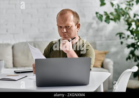 A man with inclusivity sits at his desk in a casual setting, reviewing documents and pondering his next move. Stock Photo
