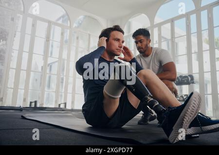 Multiracial trainer next to young man in sportswear with prosthetic leg doing push-ups at the gym Stock Photo
