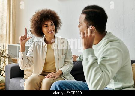 An African American couple sits on a couch, communicating with each other using sign language. Stock Photo