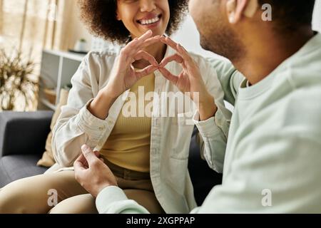 A loving African American couple communicates using sign language while sitting on a couch in their home. Stock Photo