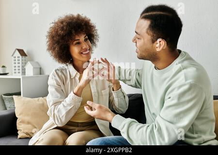 An African American couple communicates using sign language while sitting on a couch in their home. Stock Photo