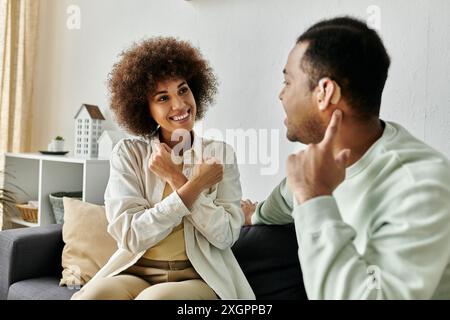 A happy African American couple communicates through sign language while sitting on a couch at home. Stock Photo