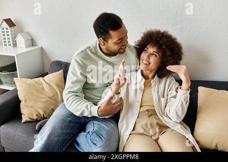 A loving African American couple sits on a couch, using sign language to communicate. Stock Photo