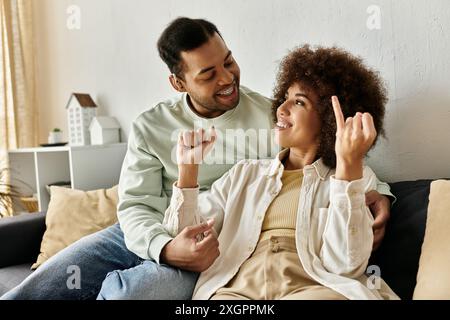 A happy African American couple communicates using sign language while sitting on a couch at home. Stock Photo