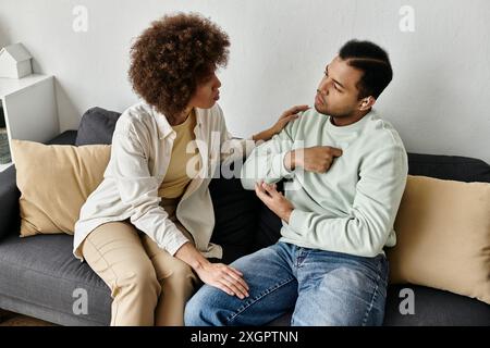 A young African American couple sits on a couch at home, communicating with sign language. Stock Photo