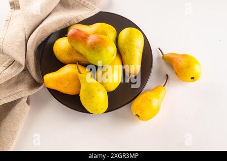 ripe yellow-green pears on plate on a white table. fresh pear closeup. Stock Photo