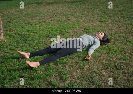 young latin woman lying on her back on grass with her arms and legs open resting after routine training and stretching to take care of her health Stock Photo