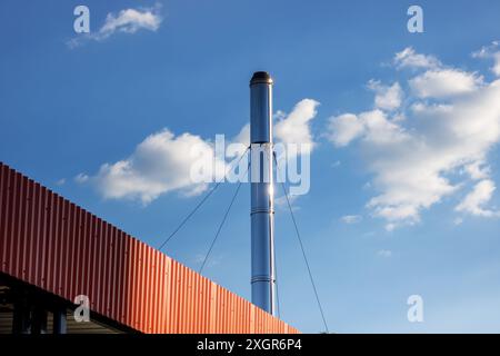 A very tall brick chimney stands out against a clear blue sky dotted with fluffy white clouds, creating a striking contrast in the cityscape Stock Photo