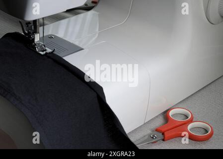 Home sewing machine close-up of the mechanism, a piece of black cloth, red scissors on the table Stock Photo