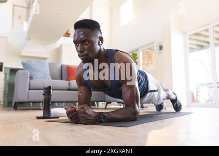 Fit african american man exercising at home, lying on floor in plank position. Fitness, training, exercise, domestic life and healthy lifestyle, unalt Stock Photo