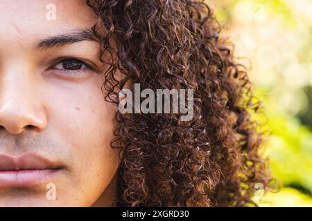 Close-up of a young biracial man outdoors, unaltered. His gaze and the natural backdrop suggest a moment of reflection or tranquility. Stock Photo