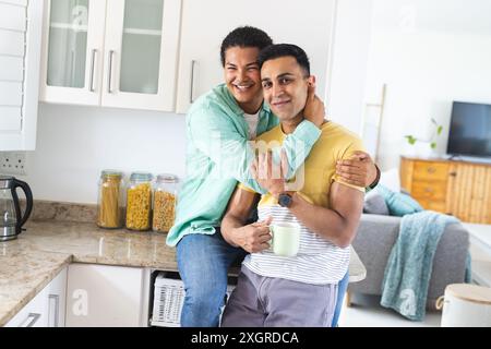 Biracial man embraces another man in a home kitchen. The gay couple shares a joyful moment, radiating happiness and comfort in a domestic setting. Stock Photo