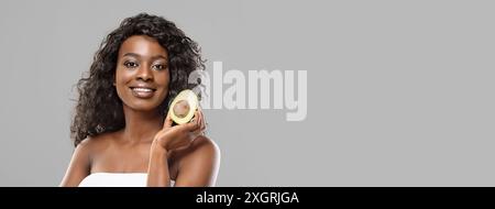 Portrait of attractive black woman with avocado half, gray background Stock Photo