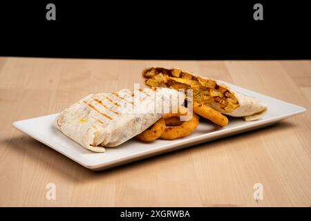 A grilled wrap filled with chicken and vegetables served with onion rings on a white plate Stock Photo
