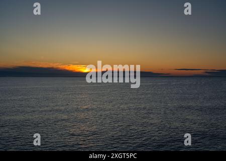 Small solitary fishing boat sails across the calm waters of the Skagerrak Sea, rising sun casting golden glow on the horizon near the coast of Norway Stock Photo