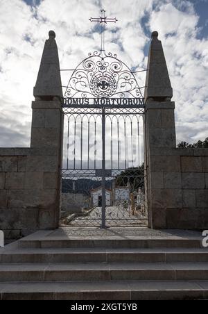 Iron gates of an old cemetery with the inscription 'Domus Mortuorum,' framed by stone pillars and steps leading up to it, under a partly cloudy sky Stock Photo