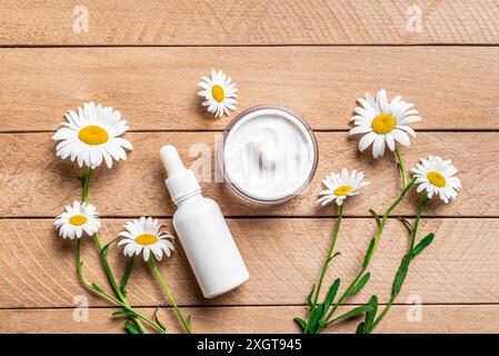 Natural organic cosmetics with chamomile flowers on wooden background, top view. Beauty cream and face serum with white daisies, organic herbal extrac Stock Photo