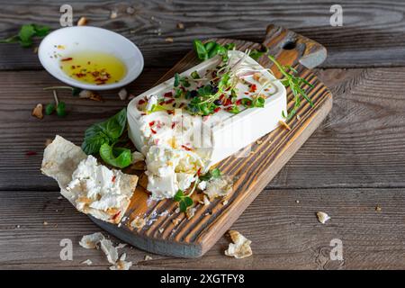 A piece of fresh feta cheese (paneer) with olives, herbs, spices and slices of flatbread (tortilla, lavash, pitta, chapatti) on a wooden board and a d Stock Photo