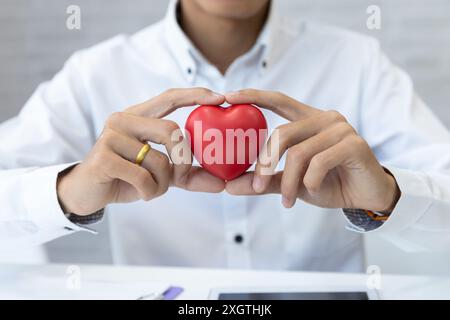 Doctor hands hold a red heart over desk. Concept of health care and medical. Stock Photo