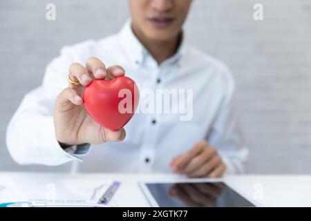 Doctor hands hold a red heart over desk. Concept of health care and medical. Stock Photo