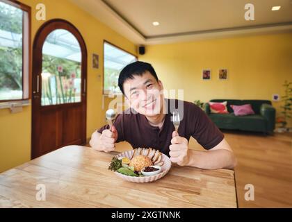 Happy asian man holding spoon and fork with crispy pork with rice in restaurant at lunch Stock Photo