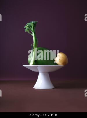 A creative display featuring a mango, potato, and broccoli stalk artfully arranged on a small, elegant white pedestal against a rich purple background Stock Photo