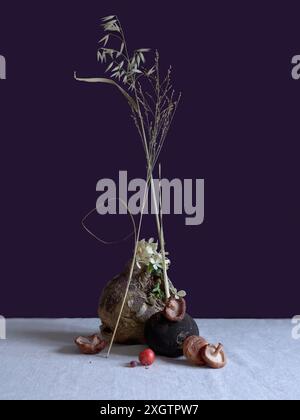 Artistic still life featuring a black radish adorned with delicate flowers, alongside shiitake mushrooms and vibrant crab apples on a textured surface Stock Photo