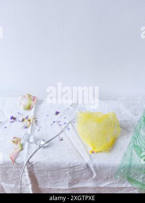 A minimalist artistic arrangement featuring dried flower petals scattered around a vivid yellow net, placed delicately on a textured white fabric, acc Stock Photo