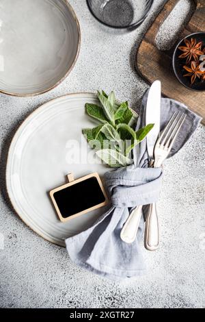 An elegant summer table setting featuring a ceramic plate adorned with fresh mint leaves, complemented by a neat linen napkin and cutlery, set on a te Stock Photo